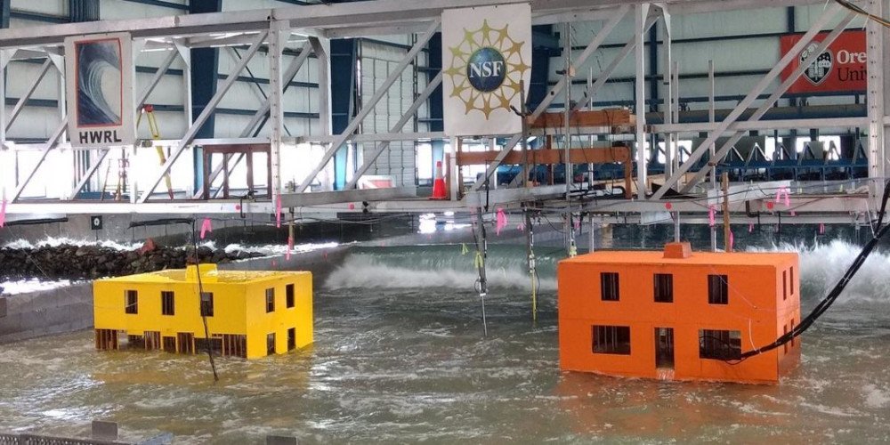 two buildings, one orange and the other yellow, submerged in a large wave testing facility 